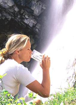 Woman Drinking Water Near a Waterfall