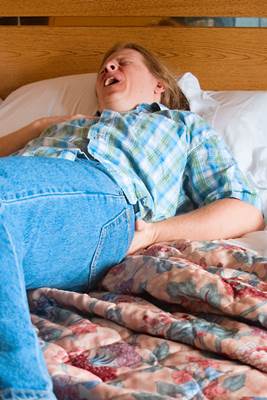Man having Acute Back Pain Lying in Bed holding His Back